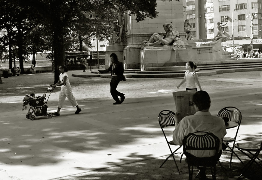 a well dressed man in a gorilla mask retrieves a fallen piece of paper for a woman pushing a stroller on a scorching hot day in central park